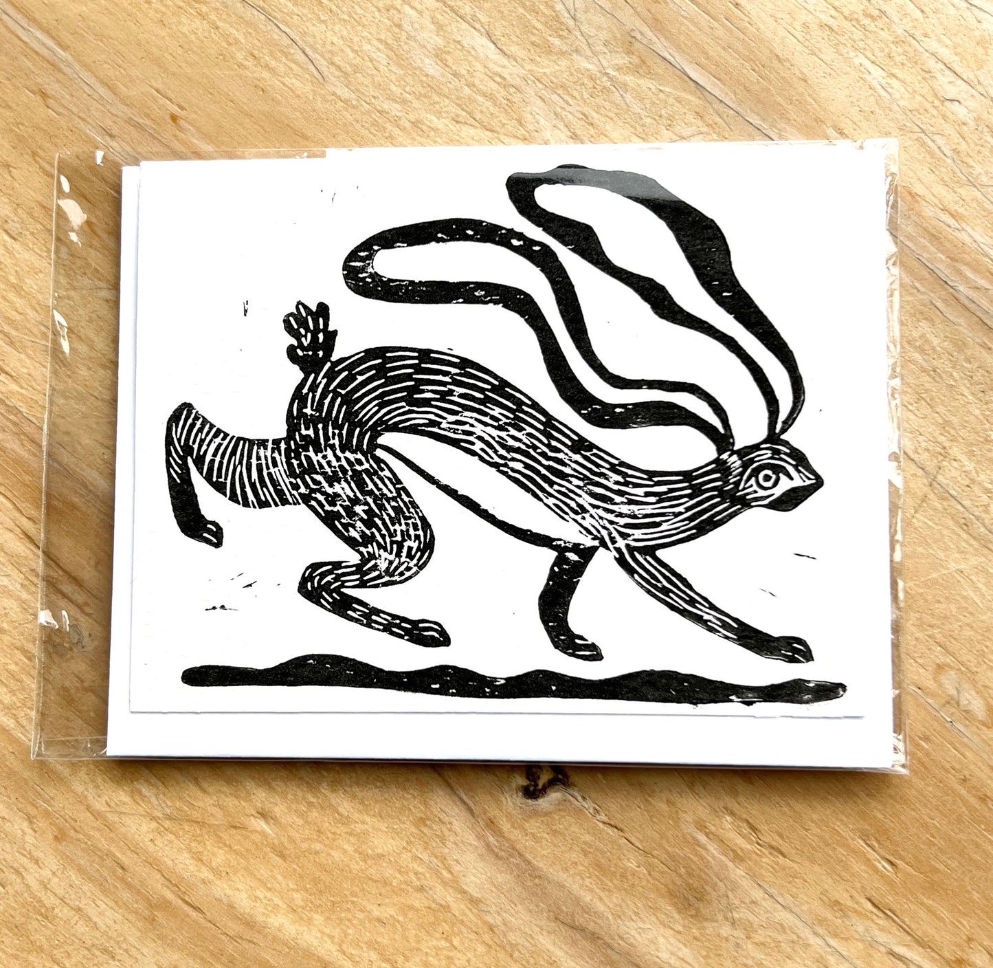 Black and white illustration of a running hare on a white card, placed on a wooden surface.