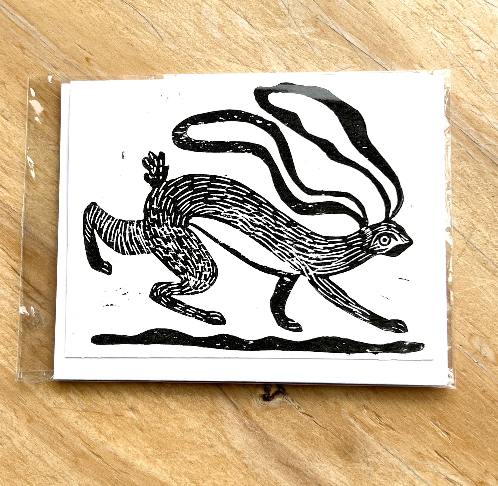 Black and white illustration of a running hare on a white card, placed on a wooden surface.